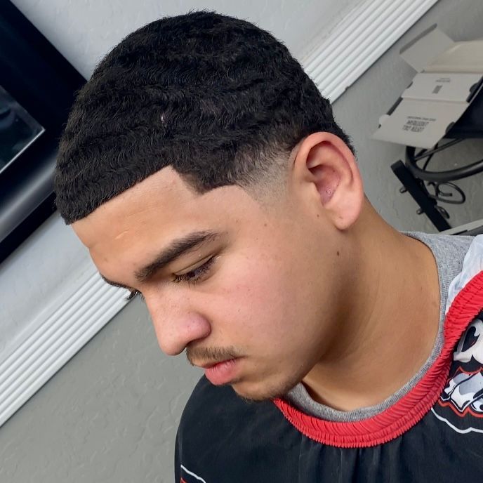 Man with waves haircut, looking down. Faded sides, thin mustache, wearing a gray and black shirt.