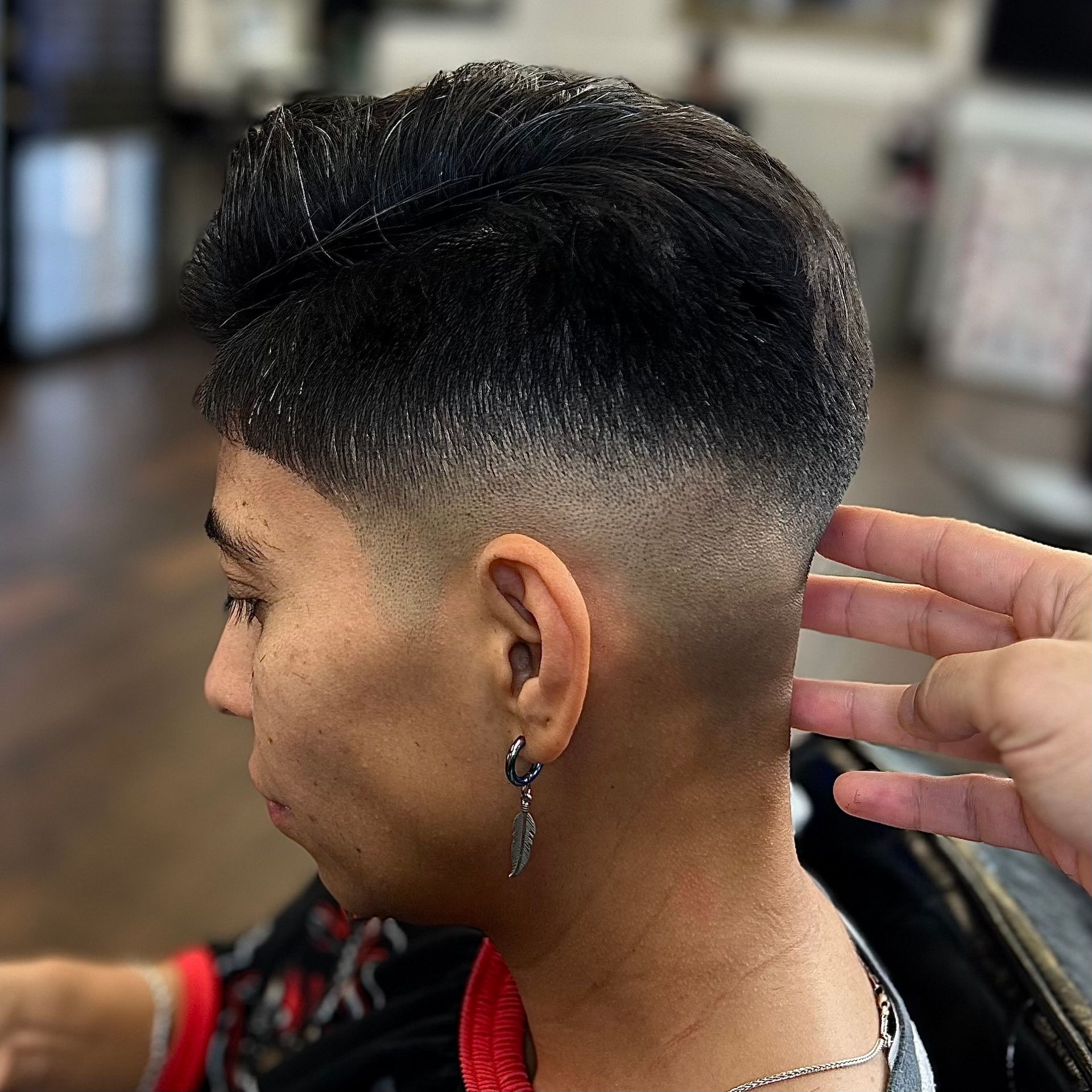 Man with dark hair and a faded haircut, getting his hair styled.