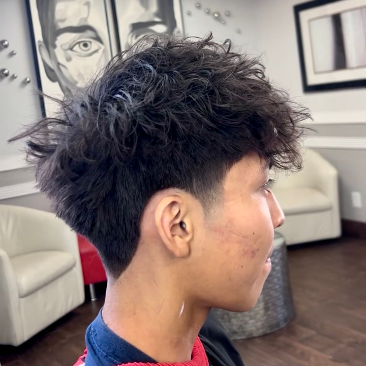 Man with messy dark hair, a high skin fade haircut, stands in a salon.