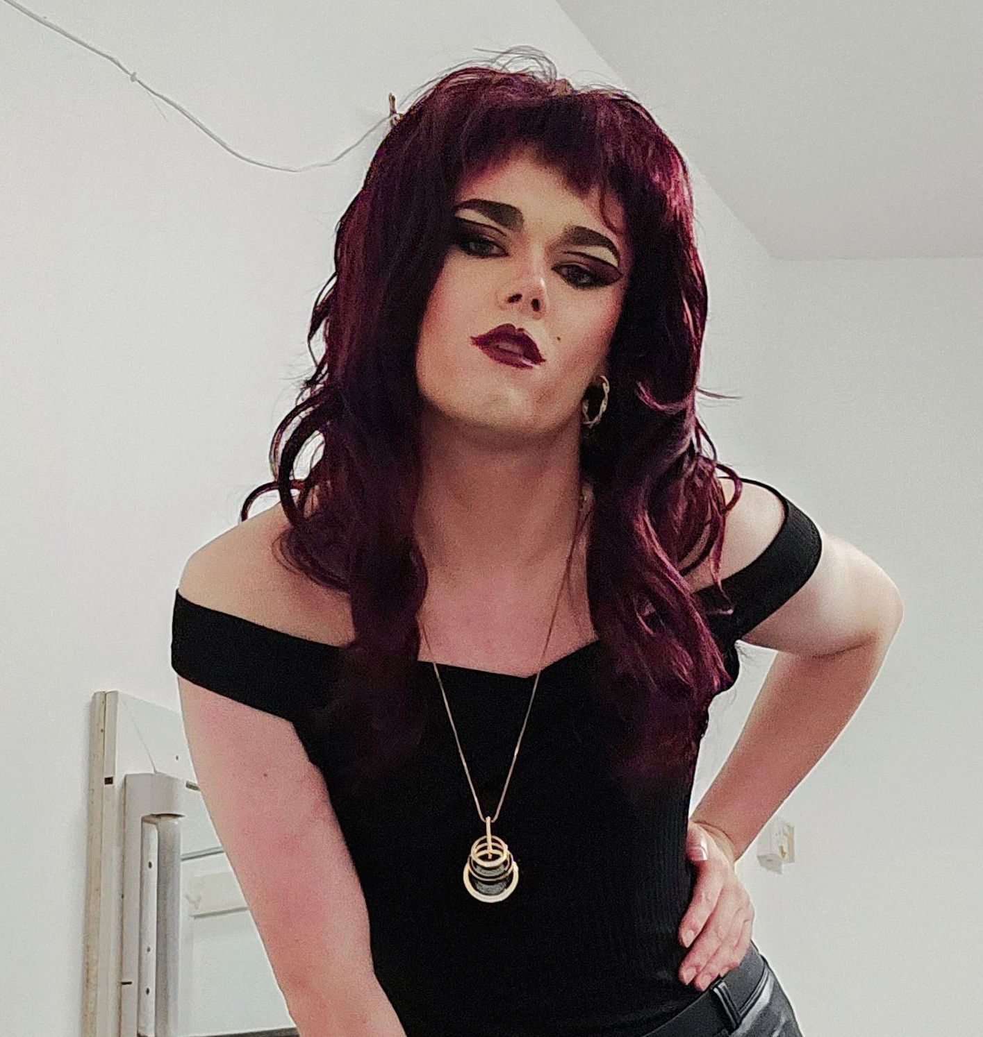 A portrait of drag queen, Object. She wears a black, off-the-shoulder  top, accompanied with 80s style make-up and blonde bombshell hair-do like Sandy from Grease the Musical.