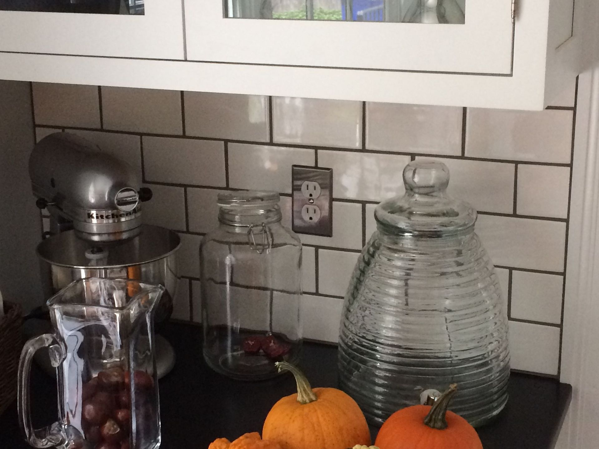 A kitchen counter with pumpkins a pitcher and a mixer