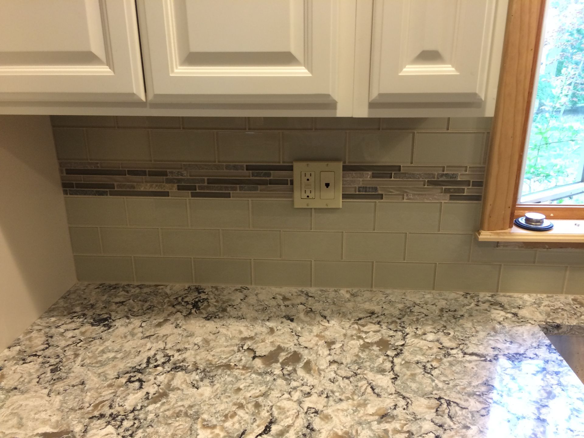 A kitchen counter with a subway tile border and a window.