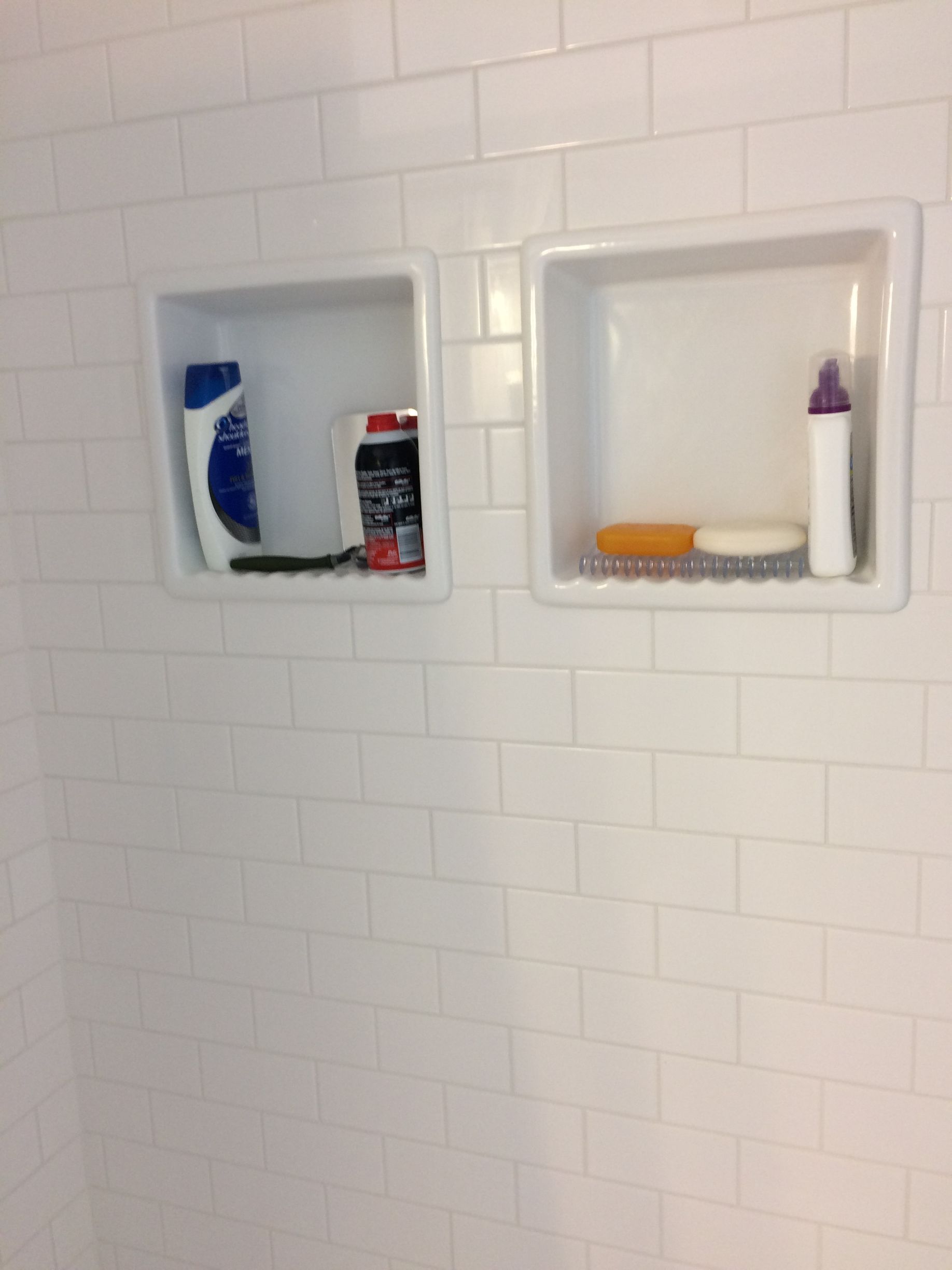 There are two shelves in the shower with bottles of shampoo and soap on them.