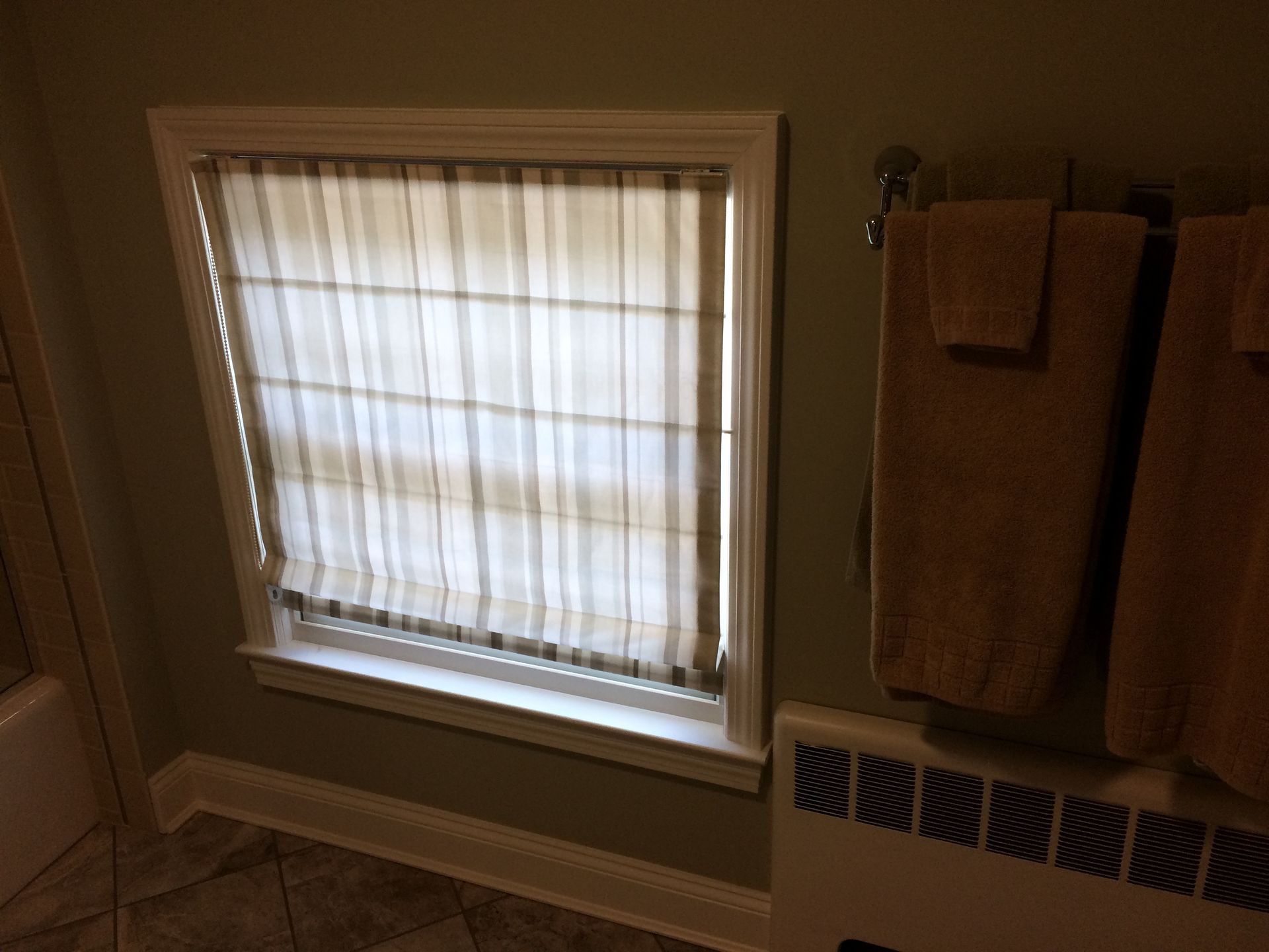 A bathroom with a window and towels hanging on the wall.