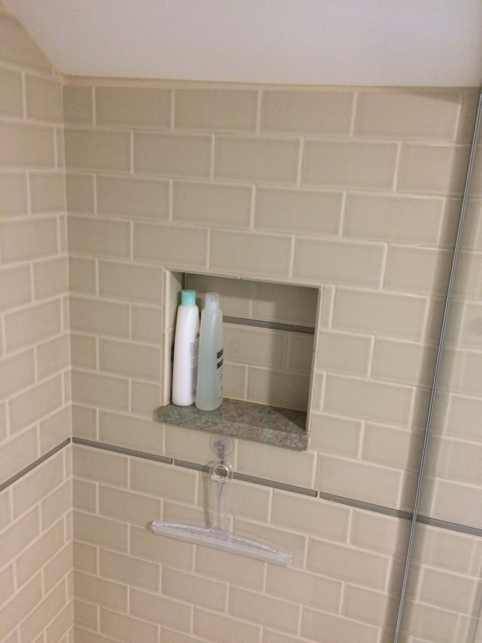 There is a shelf in the shower with shampoo and conditioner on it.
