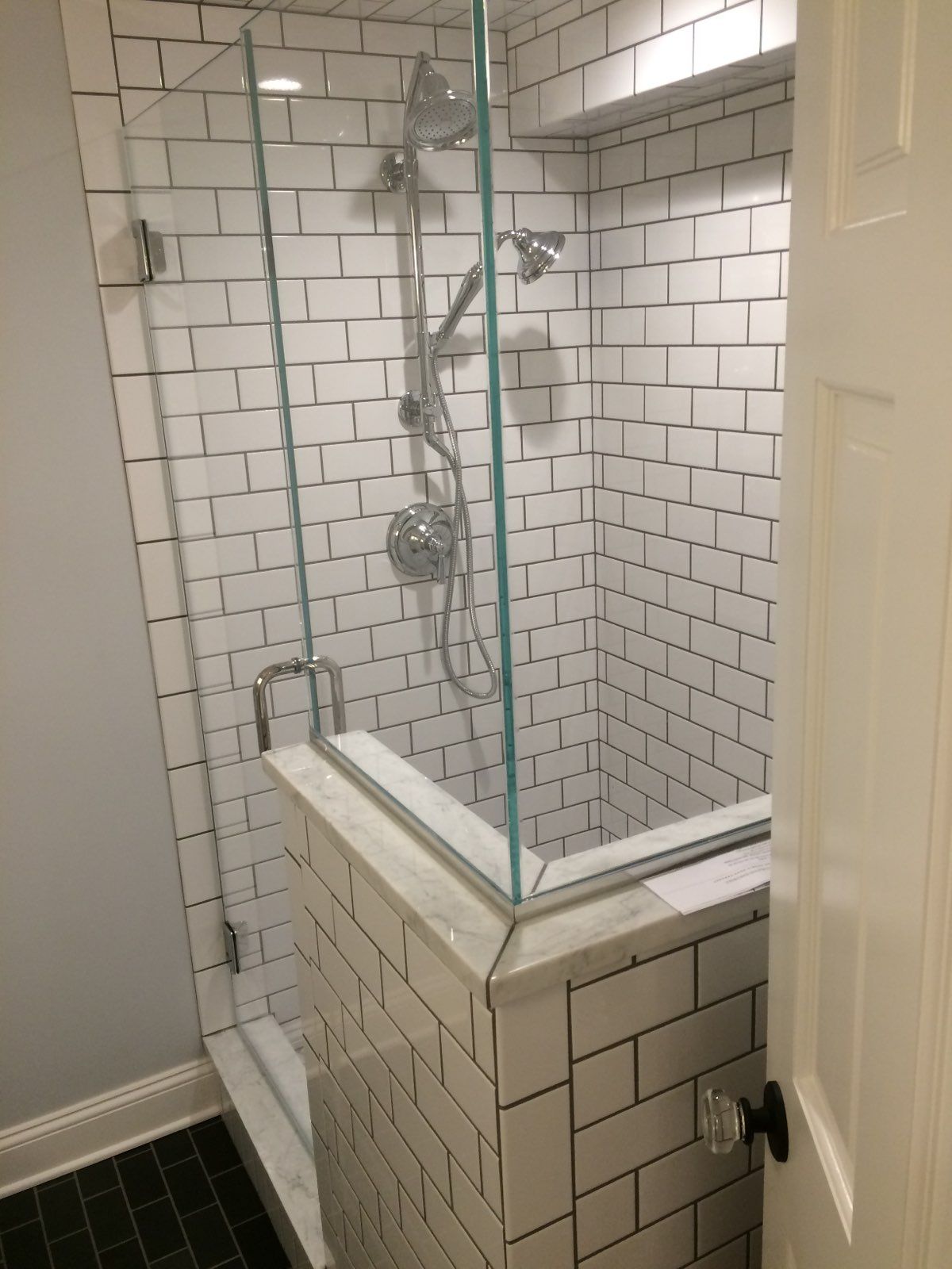 A bathroom with white brick walls and a walk in shower with a glass door.