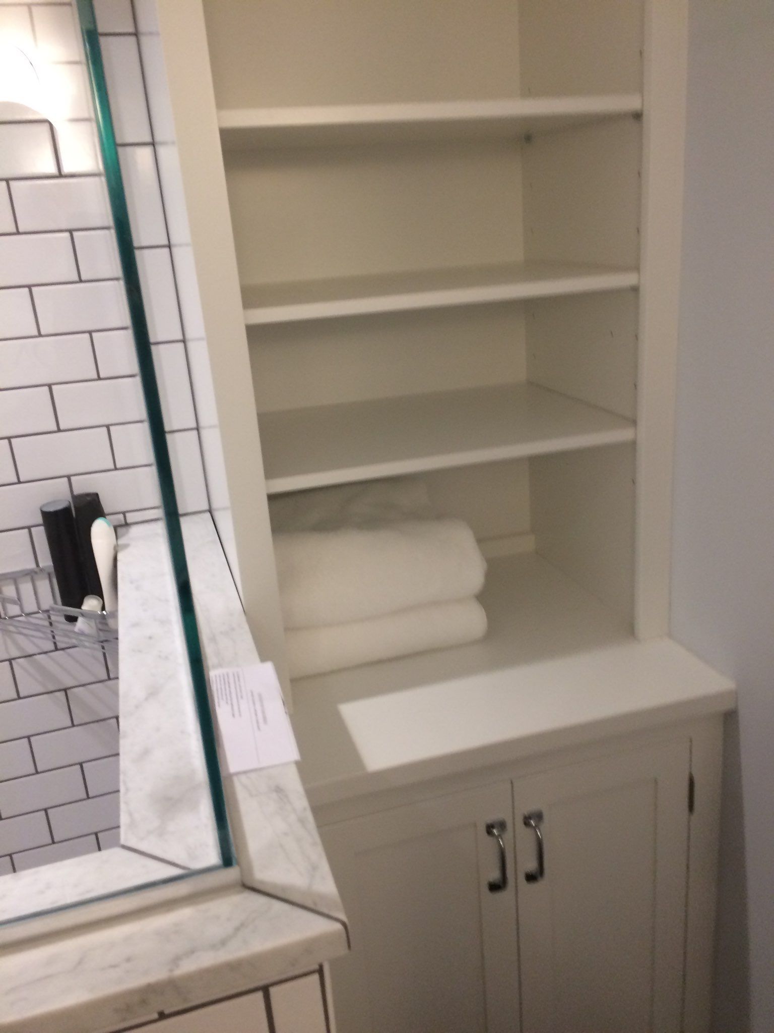 A bathroom with white cabinets and shelves and a mirror