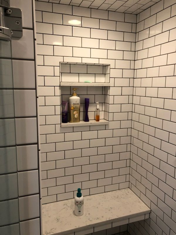 A bathroom with white bricks and a shelf with bottles on it