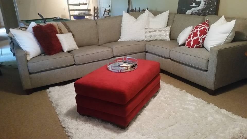 A living room with a sectional couch and a red ottoman