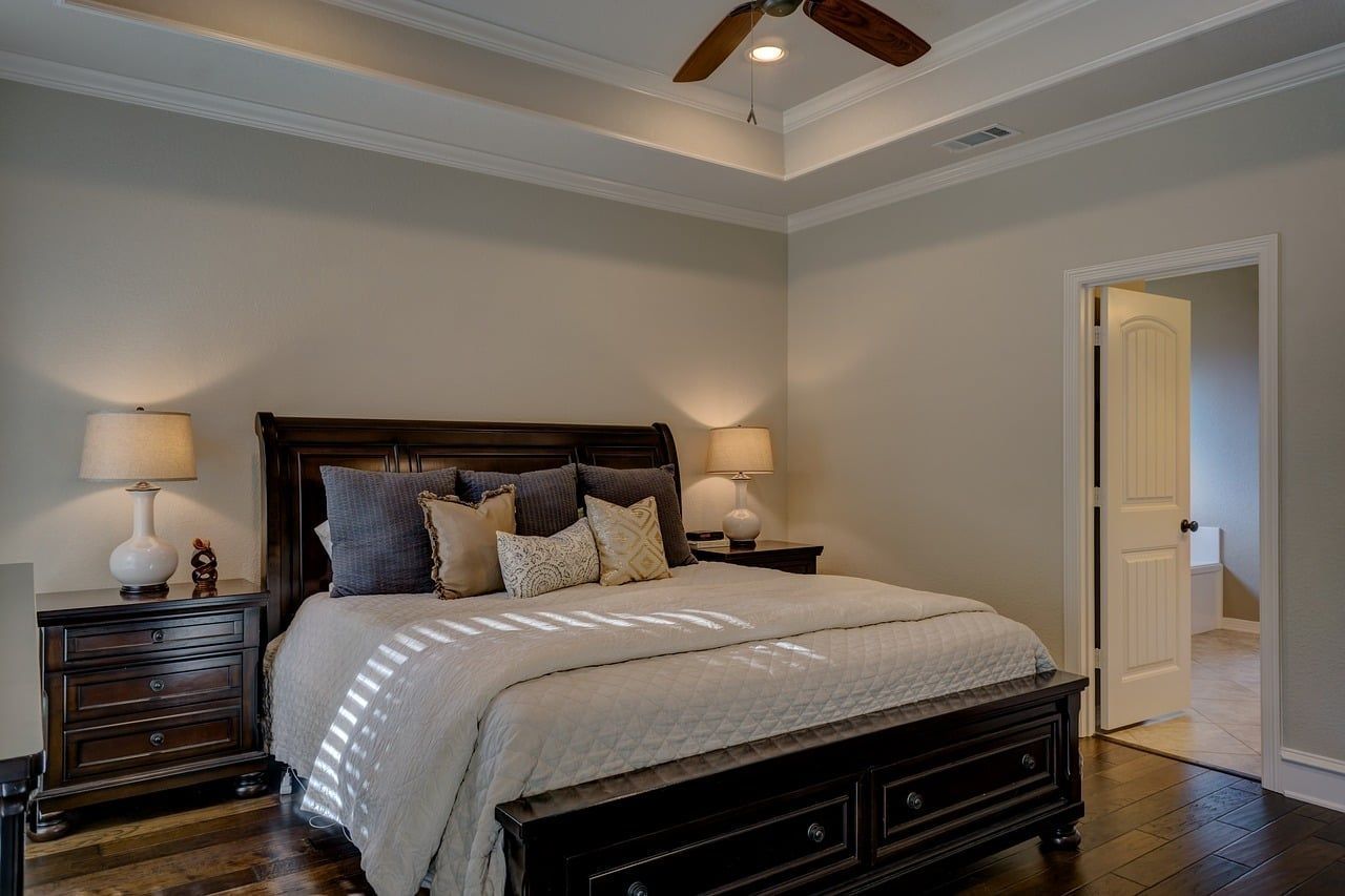 A bedroom with a bed , nightstands , lamps and a ceiling fan.