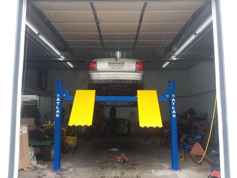 A car raised on a blue and yellow Atlas lift inside a garage.