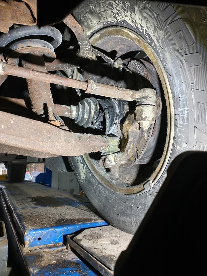Car's front wheel on a lift, showing a leaking CV joint covered in grease.