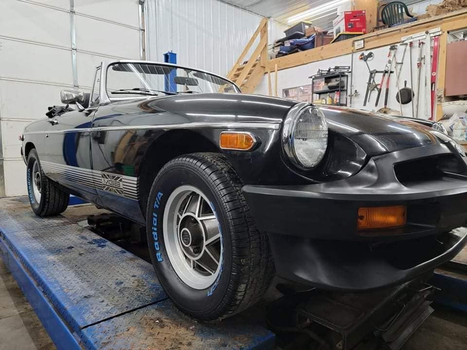 Black MG convertible on a blue car lift inside a garage.