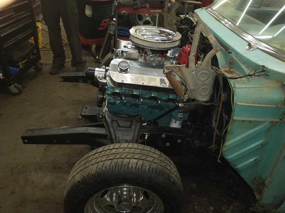 Blue engine installed in a vintage car frame with a tire. Workshop setting.