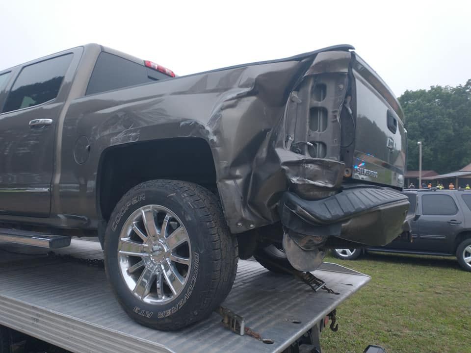 Damaged gray pickup truck, rear end crumpled, being towed on a flatbed.
