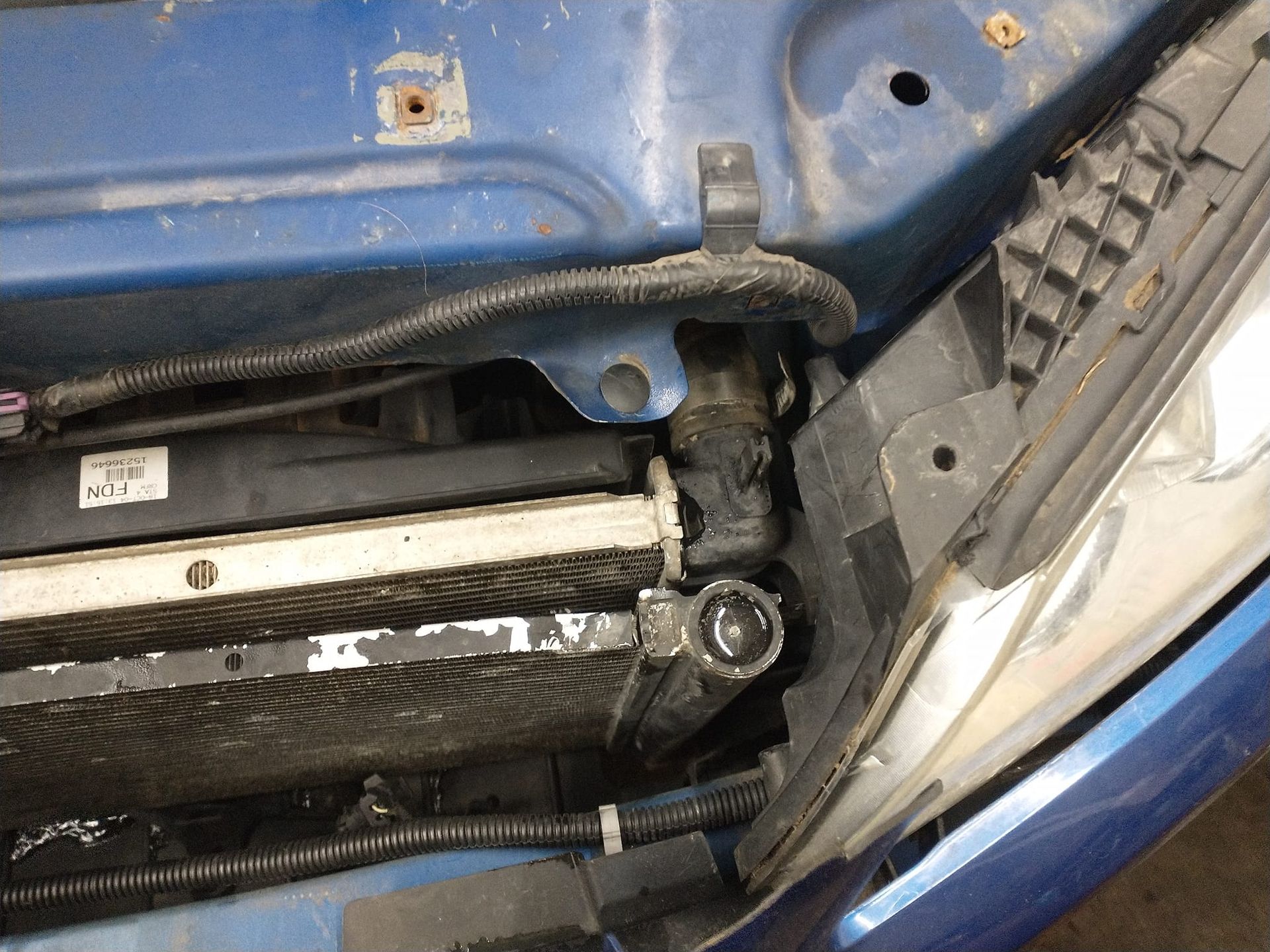 Blue car engine bay showing a radiator and surrounding parts, some with corrosion.