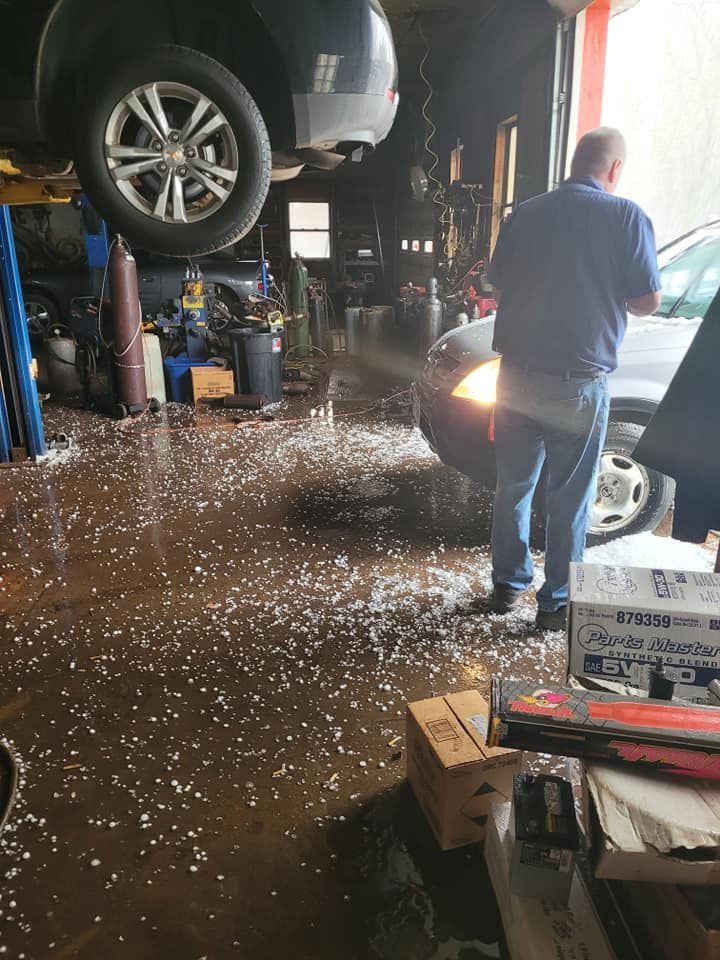Car in repair shop, floor covered in white debris. Man standing near car.