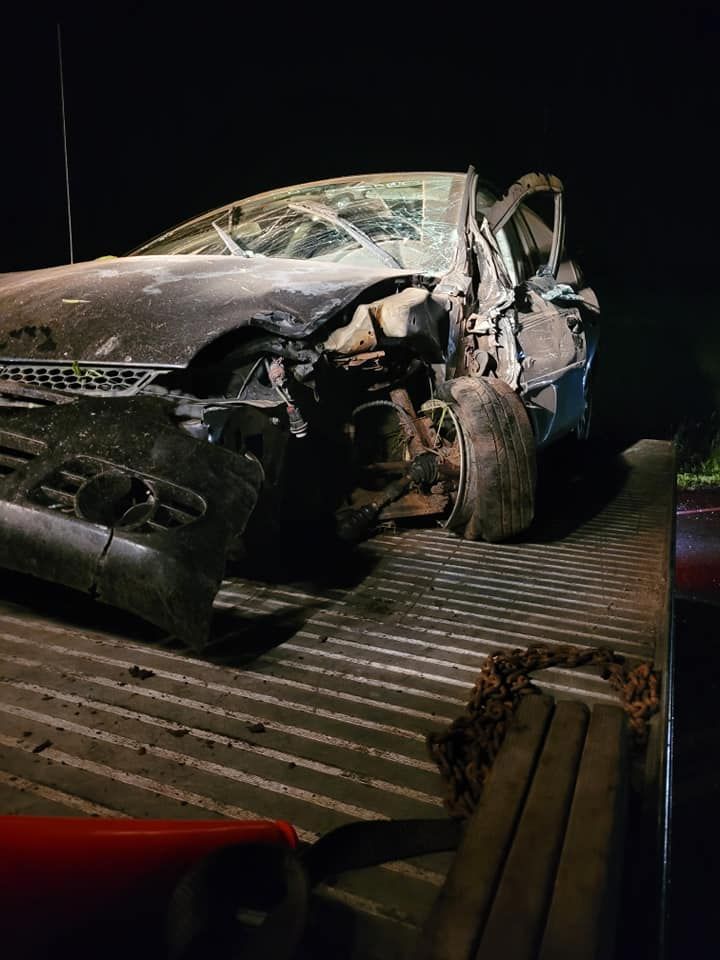 Damaged vehicle on a tow truck at night; front end is severely wrecked.