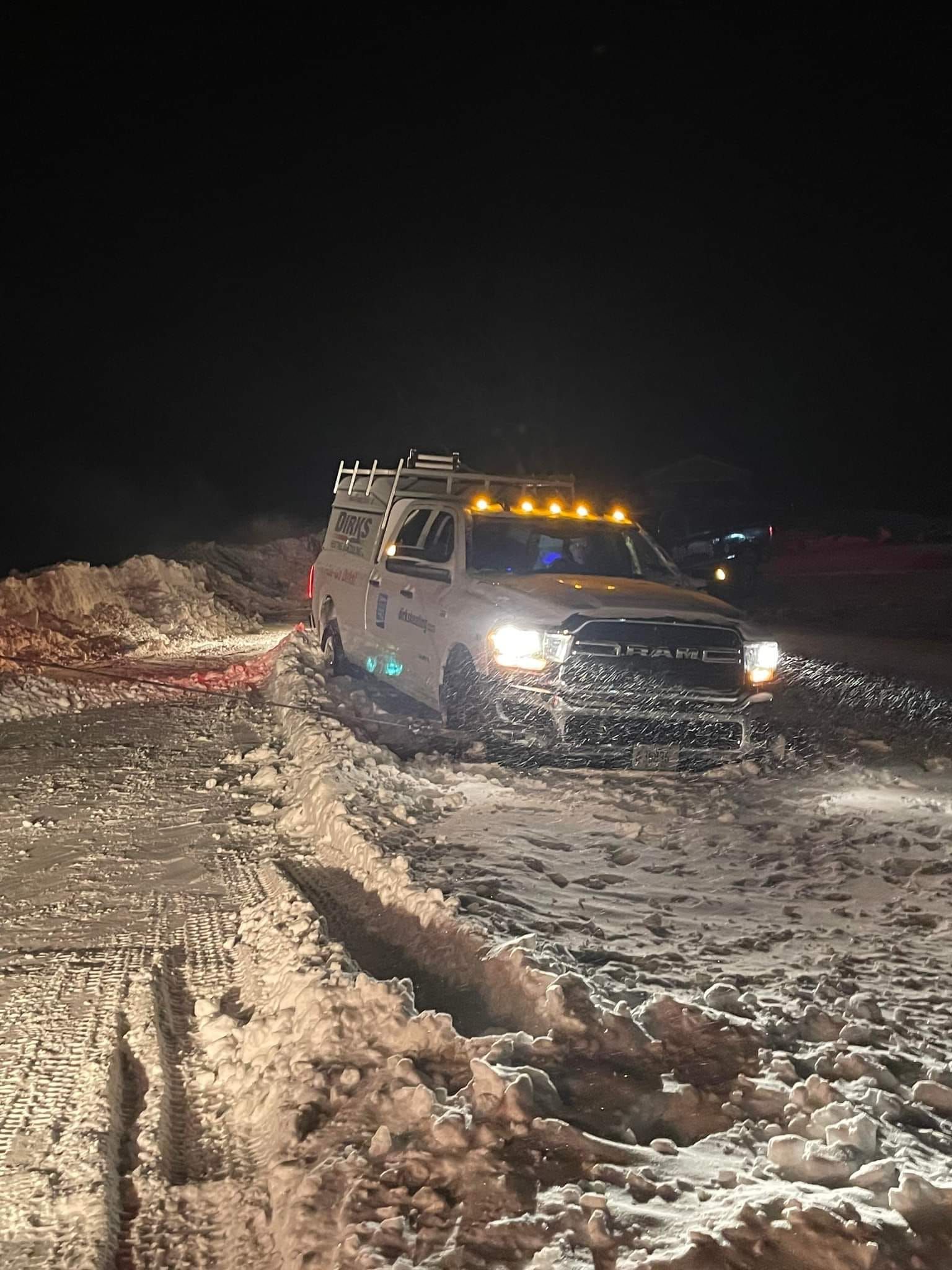 White truck driving through snow at night. Headlights on, lights on top.