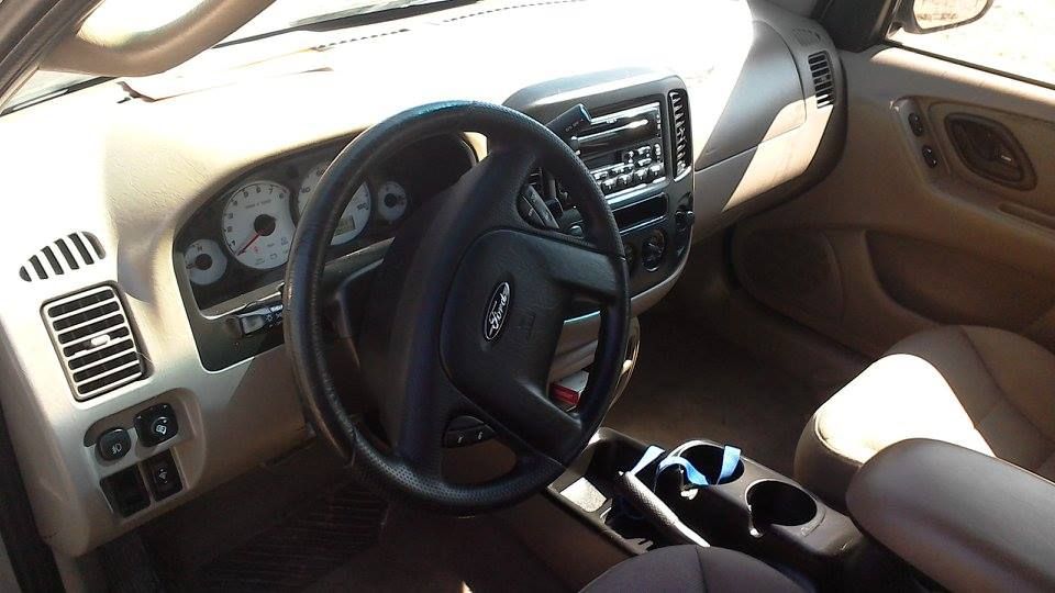 Beige car interior, dashboard with steering wheel, gauges, and radio. Cup holders in center console.