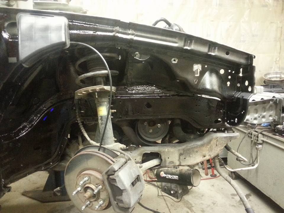 Black vehicle chassis, front end partially disassembled, brake rotor visible.