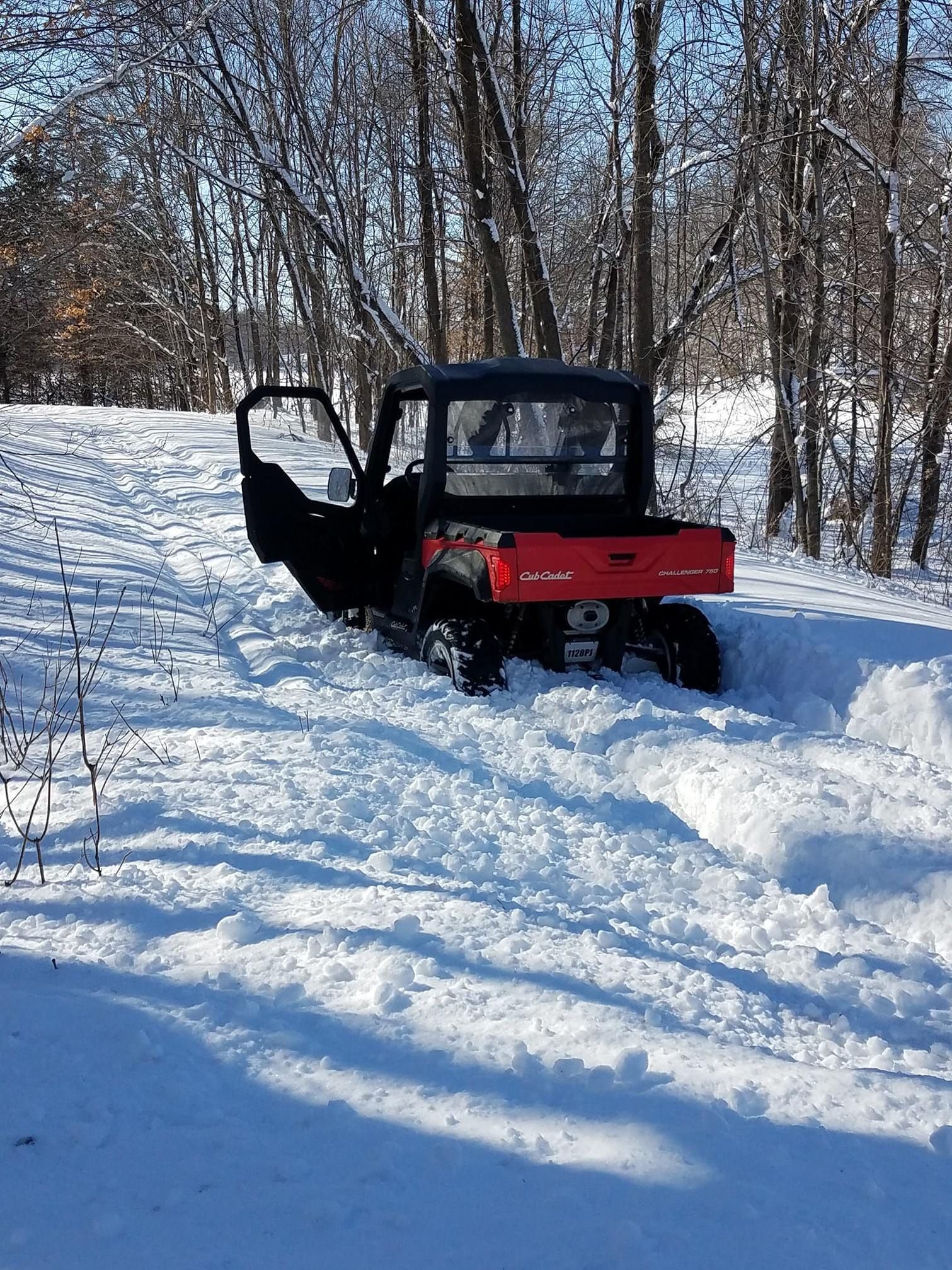Red and black UTV stuck in deep snow, door open, in a snowy, wooded area.