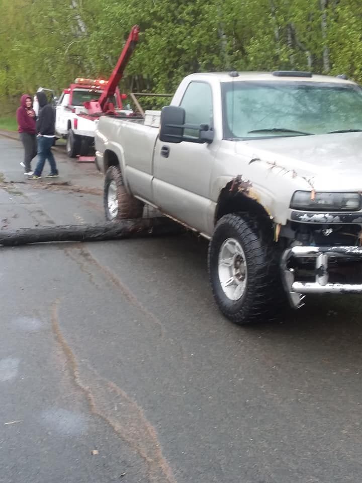 A light silver pickup truck stuck on a log in a road. A tow truck is behind it.