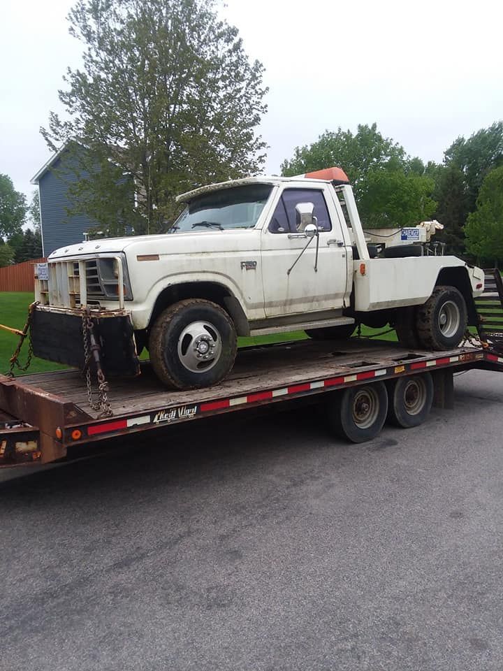 White tow truck on a flatbed trailer, parked on pavement, with a residential background.