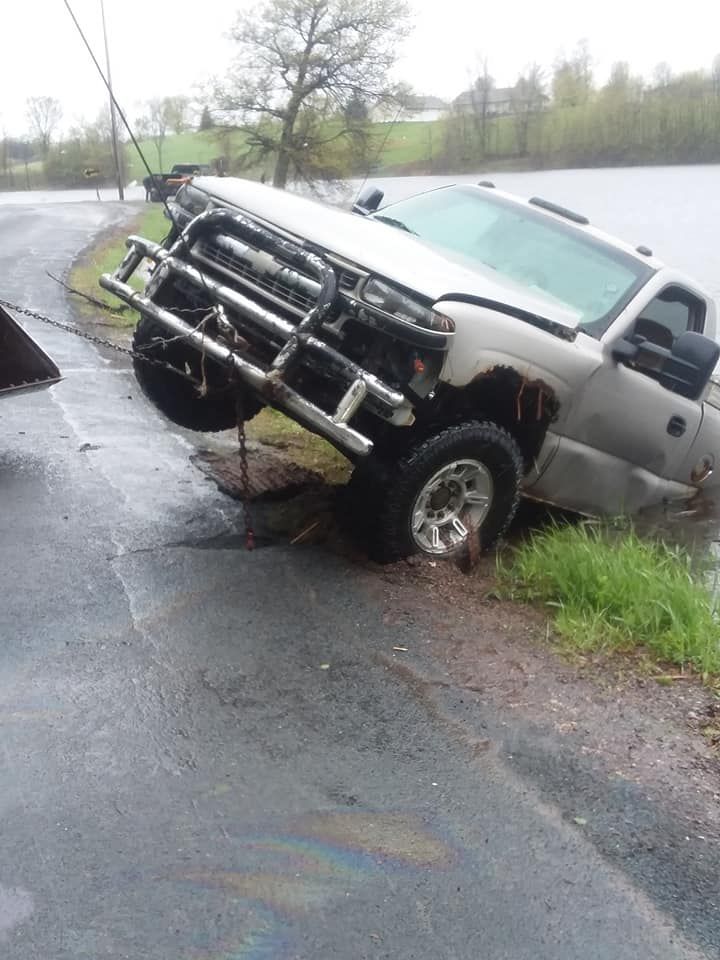 Silver pickup truck partially submerged in water, on a wet road, leaning toward the right.