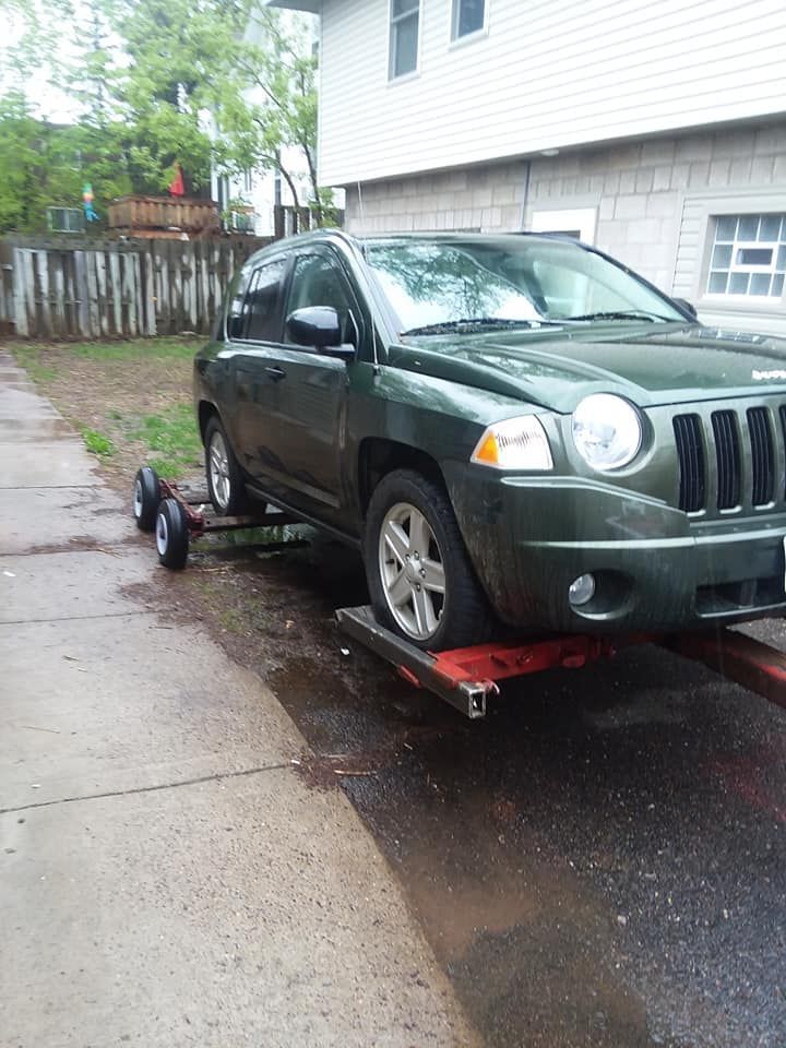 Green Jeep Compass on a tow dolly in a residential driveway.