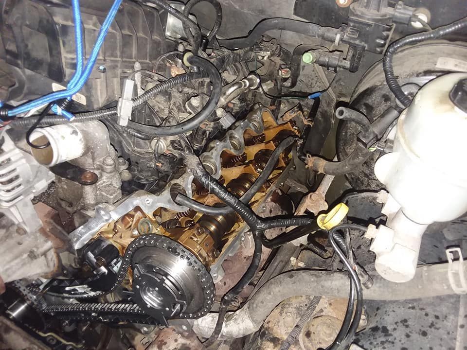 Engine compartment with disassembled parts; oily, metal, and plastic components visible.