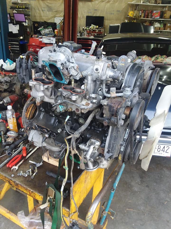 A disassembled car engine sits on a yellow workbench in a garage.
