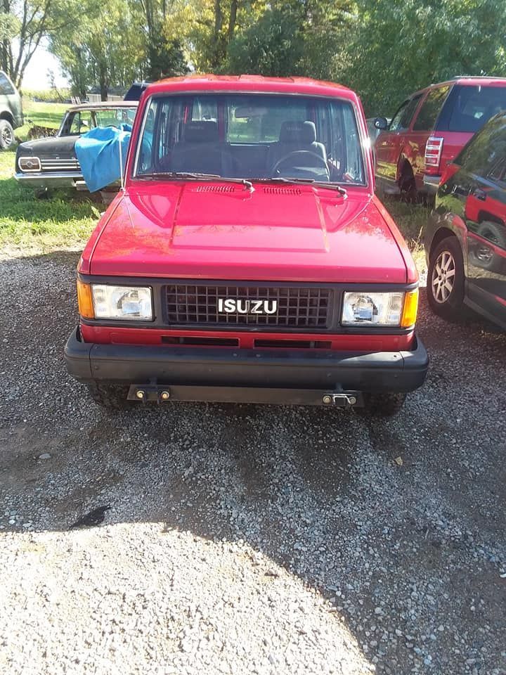 Red Isuzu Trooper SUV, parked on gravel, facing forward. Sunny day.