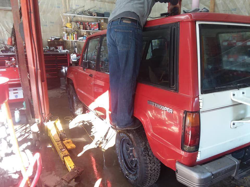 Person standing on a tire of a red SUV in a garage, reaching upwards.
