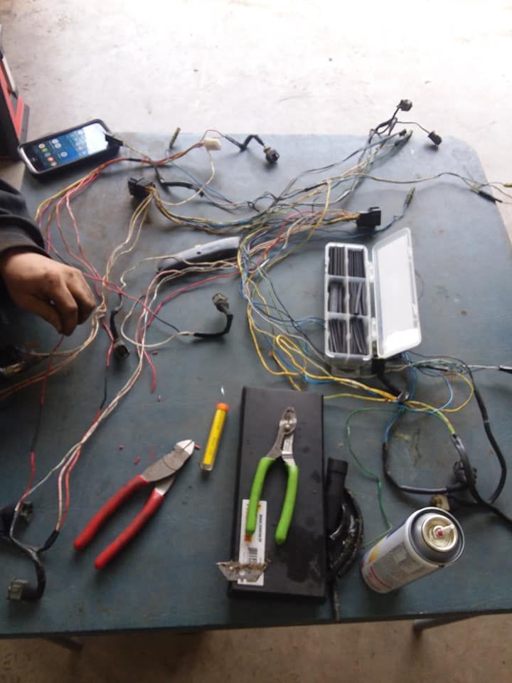 Person working on a car wiring harness on a table, with tools, wires, and a phone.