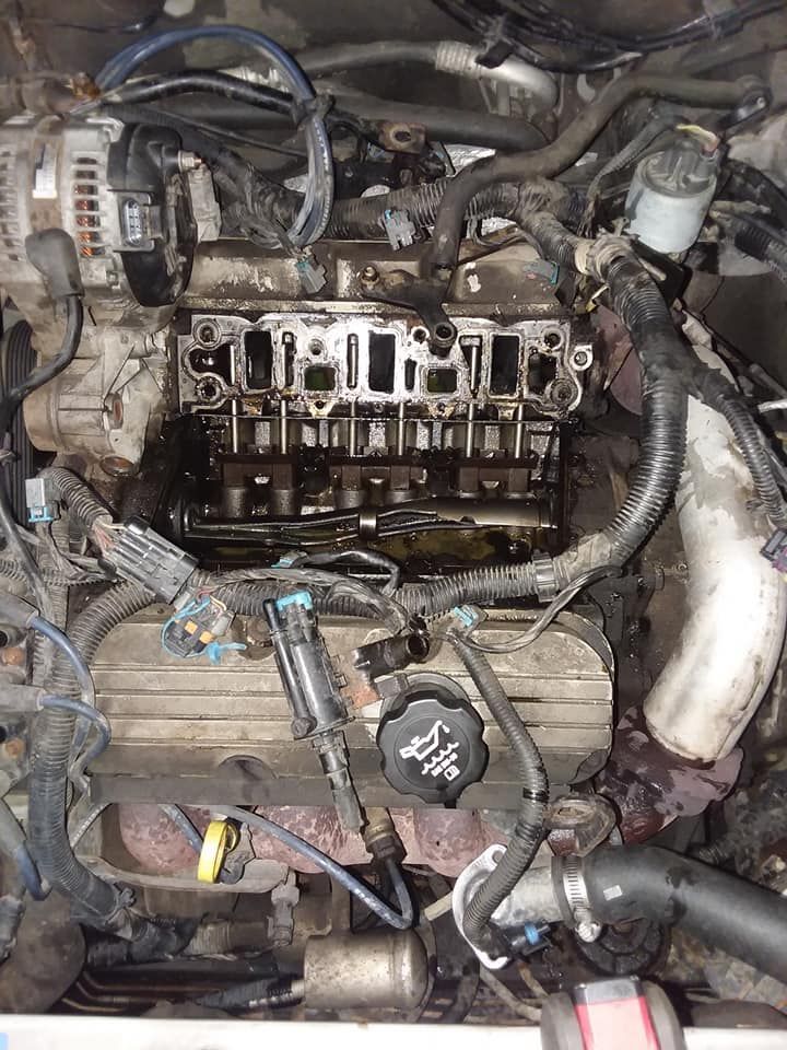 Car engine with exposed components, oil staining, and various wires and hoses.