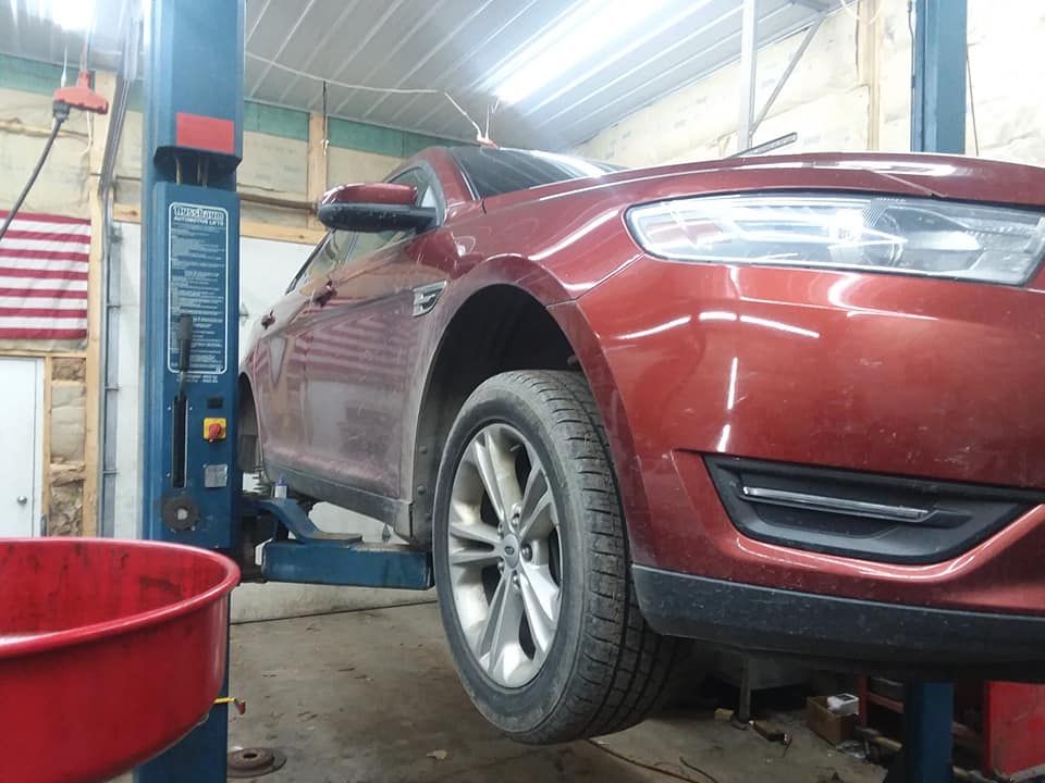 Red car raised on a lift in a garage, likely for repair. A red container sits below.