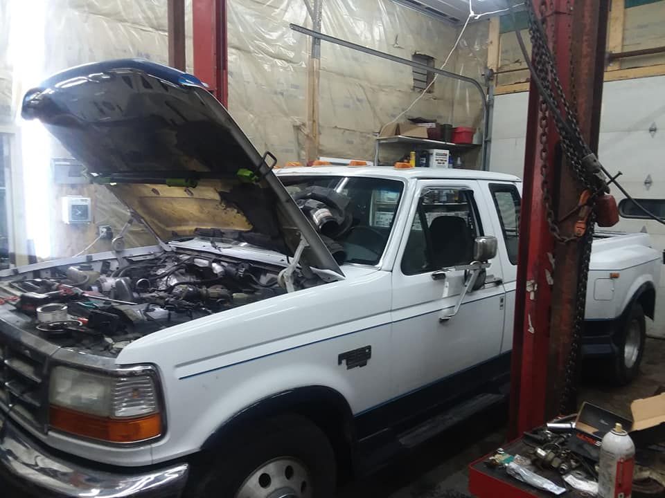 White Ford pickup truck with open hood in a garage, under a lift.