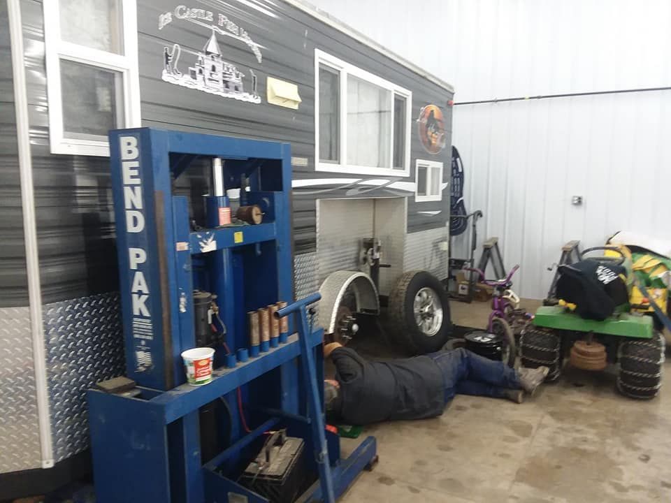 Man working under vehicle near an ice fishing house and a Bend Pak machine.