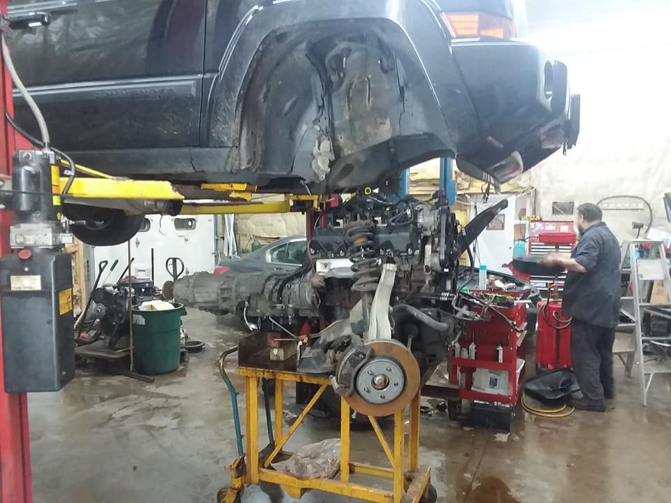 Jeep on a lift, engine removed, mechanic working in a repair shop.