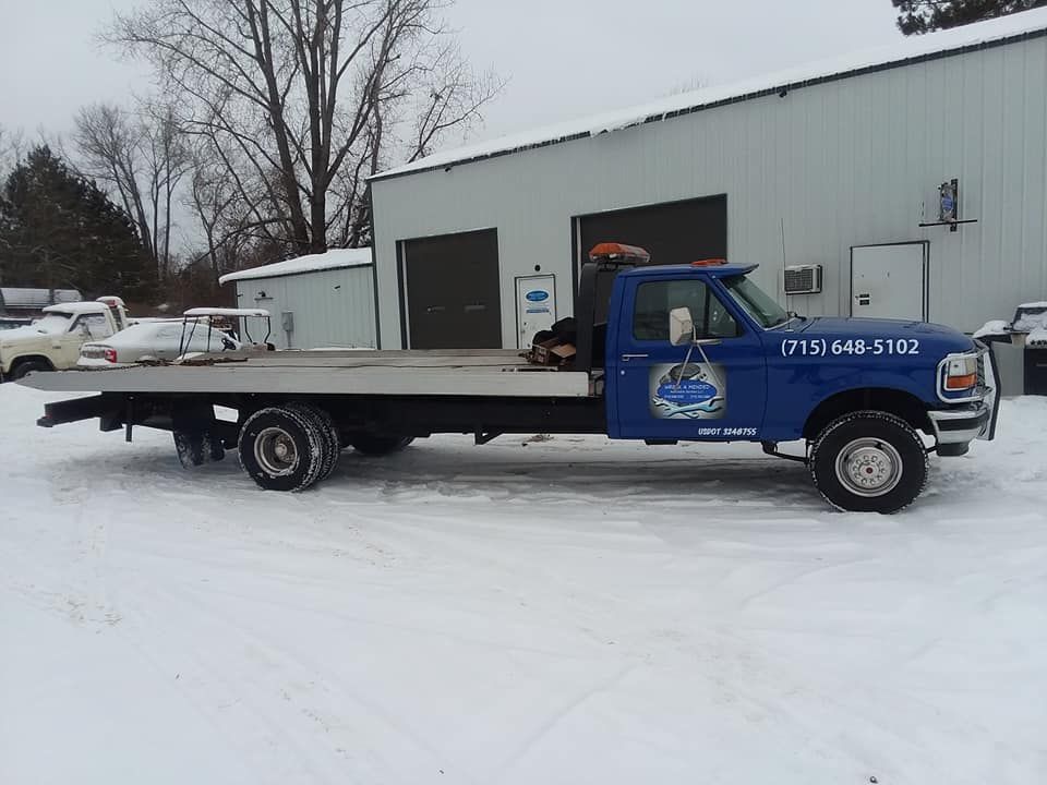 Tow truck with an empty flatbed in the snow in front of a building.