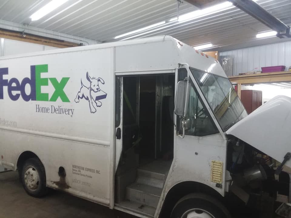 FedEx delivery truck parked in a garage, driver's side door open, hood up.