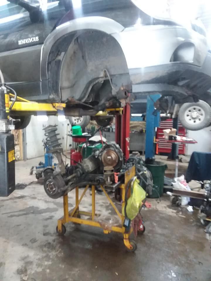 Front end of a car being repaired in a shop, with parts on a rolling cart below.