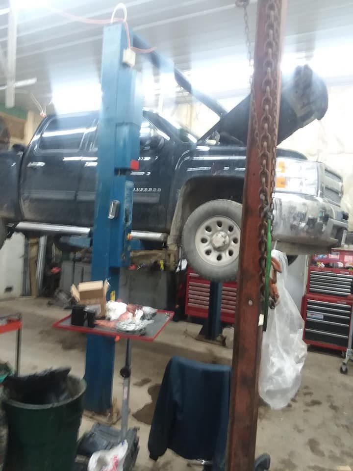 Black pickup truck raised on a car lift in a garage with open hood; tools and equipment visible.