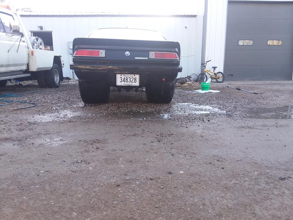 Black classic car parked in front of a garage, wet pavement.