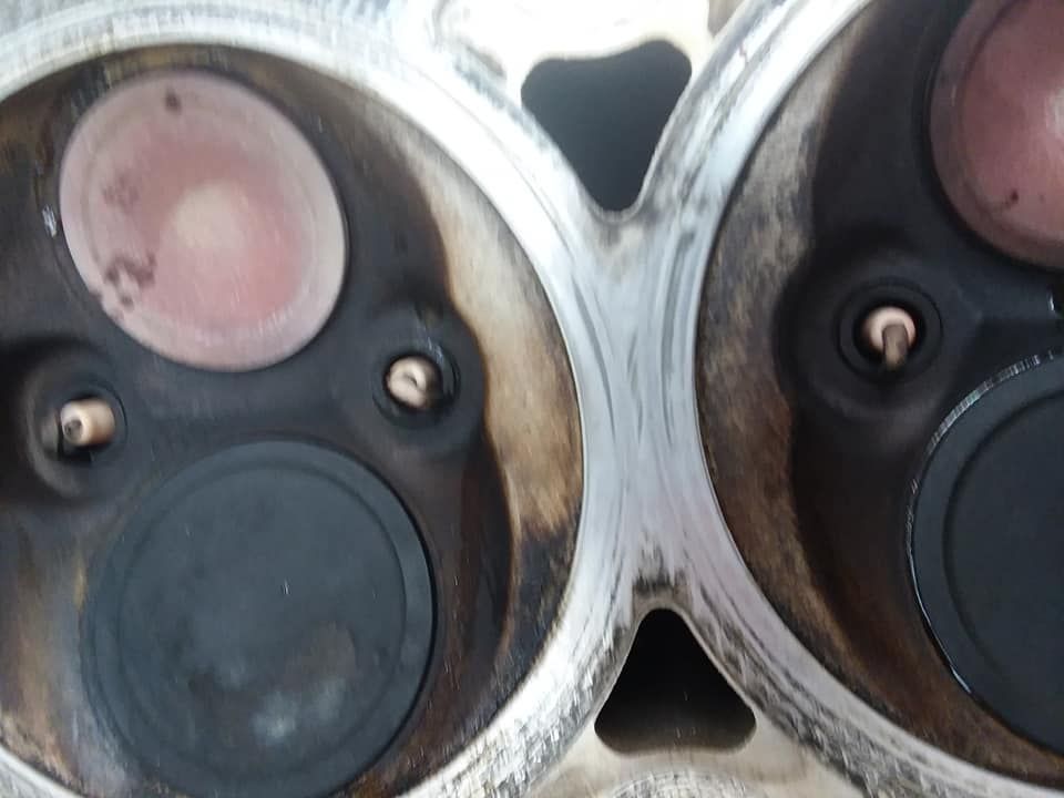 Close-up of a cylinder head showing two valves, black and pink, surrounded by dark deposits.
