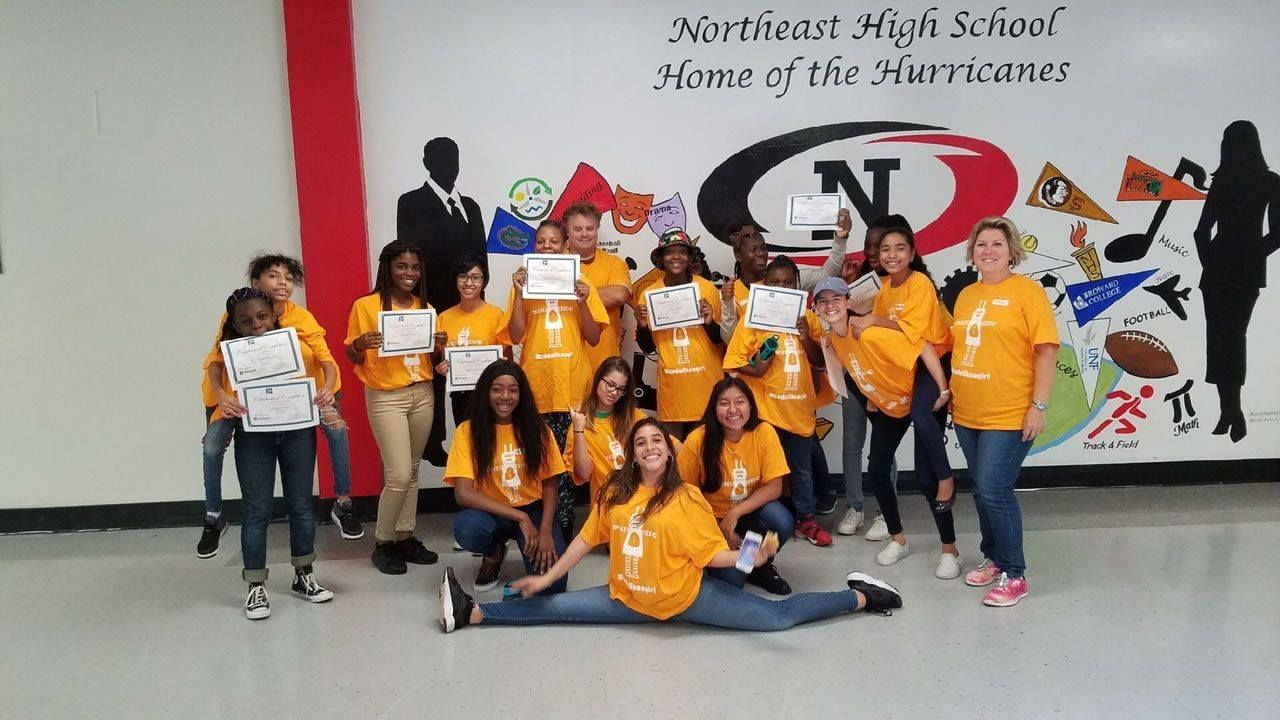 Group of students in orange shirts posing in a school hallway with a wall mural behind them
