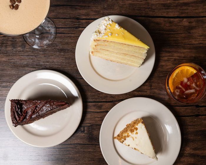 Overhead view of three dessert slices and iced tea on white plates on a wooden table