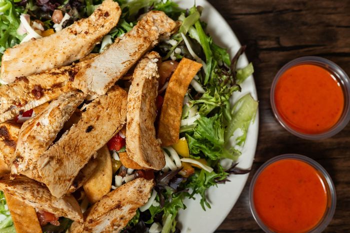 Grilled chicken breast over mixed greens with two red dipping sauces on a white plate