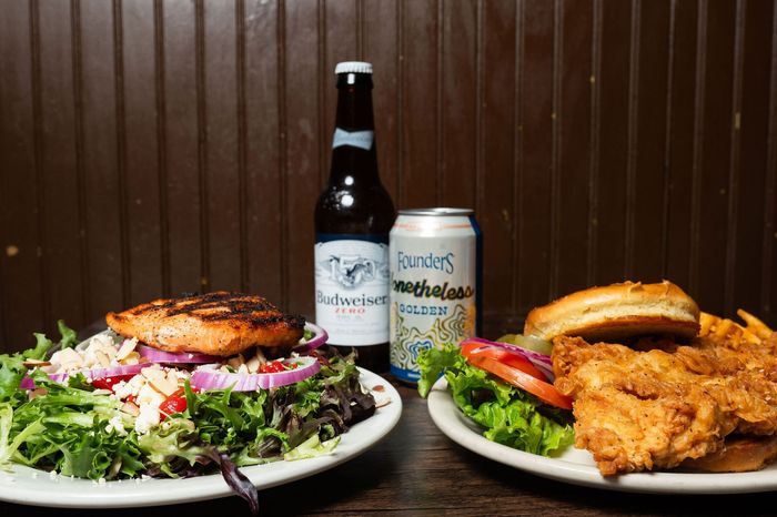 Burger, fried chicken sandwich, salad, and bottled beer and soda on a table.
